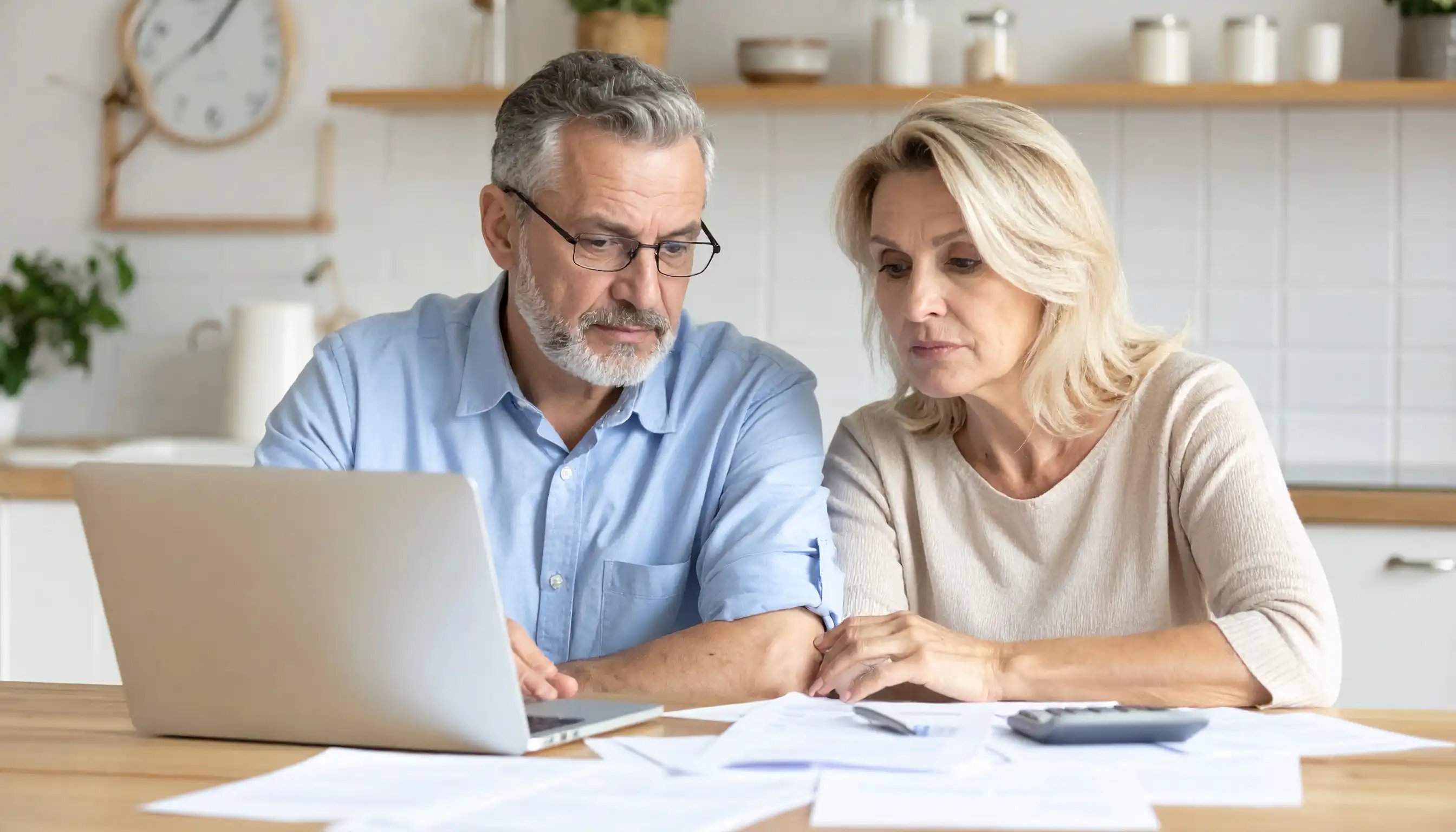 Ehepaar sitzt am Esstisch vor dem Laptop, umgeben von Unterlagen