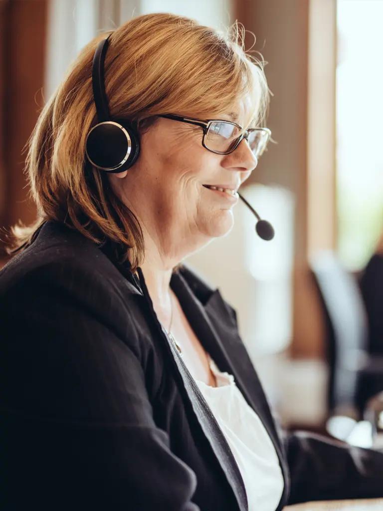 Frau mit Headset lächelnd telefoniert mit Mandanten
