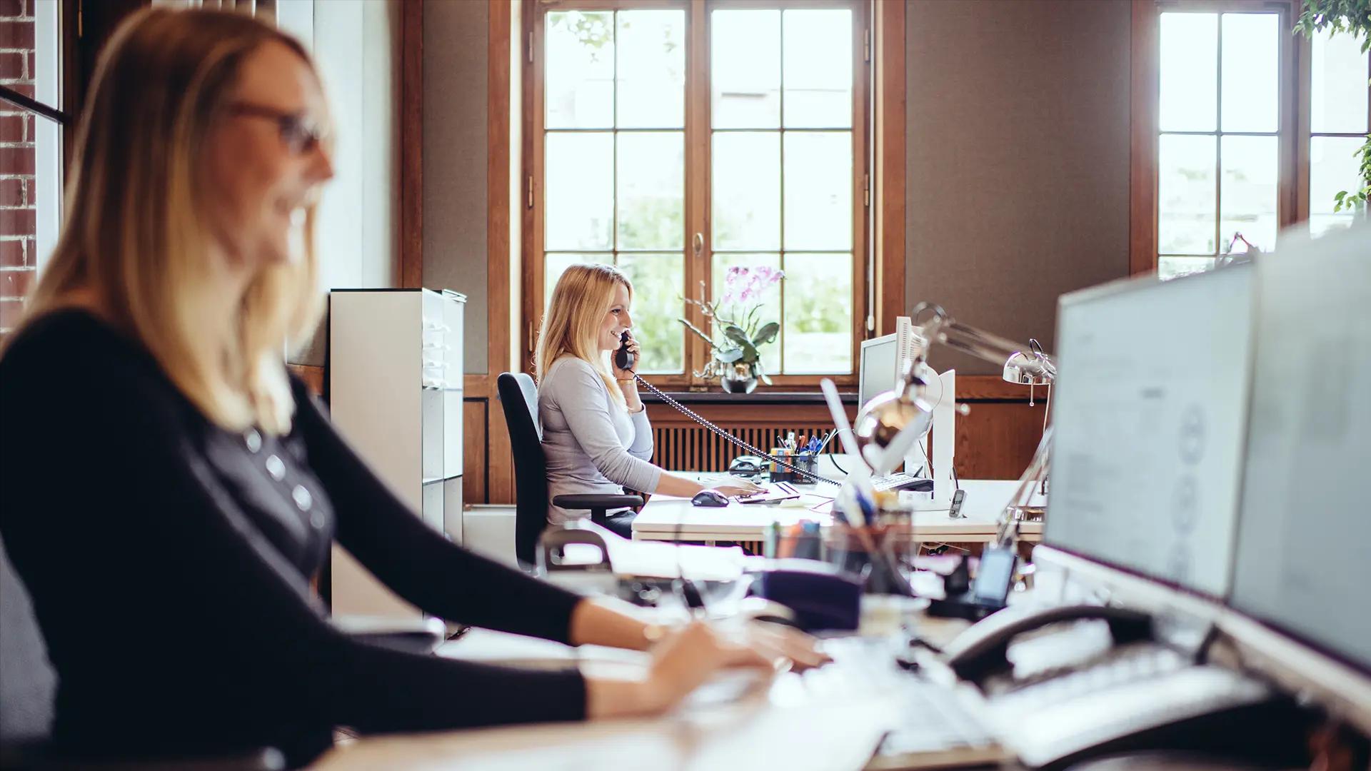 AdvoNeo Mitarbeiterinnen telefonieren und beantworten Mails am Arbeitsplatz