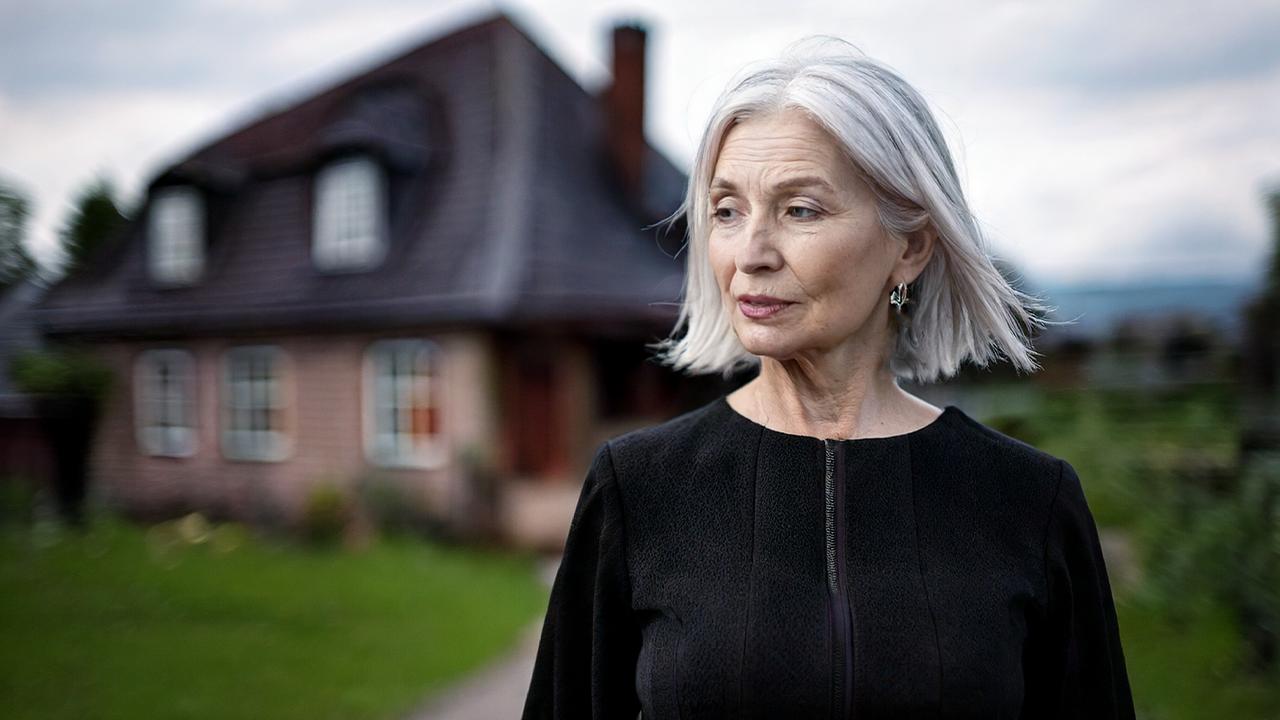 Haus mit Schulden erben im Trauerfall (Symbolbild): schwarz gekleidete, besorgte Frau steht vor Haus