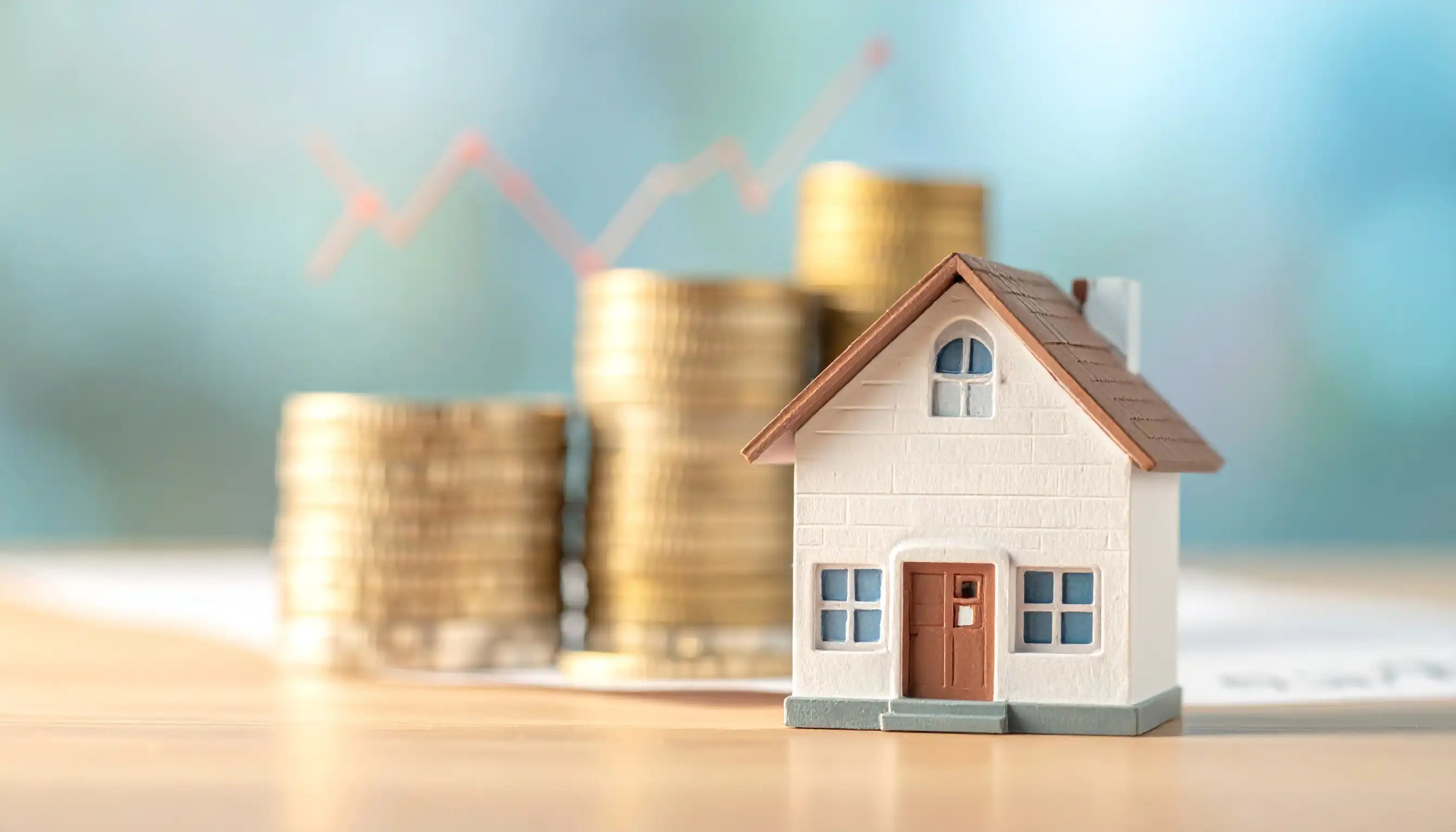 Ein kleines Modellhaus steht vor einem Stapel Münzen und Finanzdokumenten.